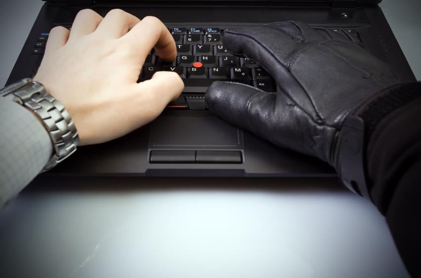 Employee using laptop. One hand bare, the other with a glove to symbolize fraudulent activity.